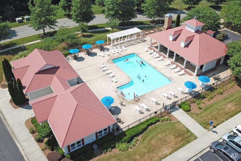 Aerial view of Ashbury Square featuring a pool and a red-roofed building surrounded by greenery.