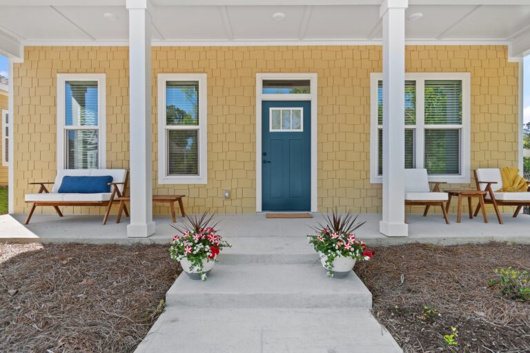 A yellow house with a blue front door and white columns, labeled as Heartsease at Shallotte.