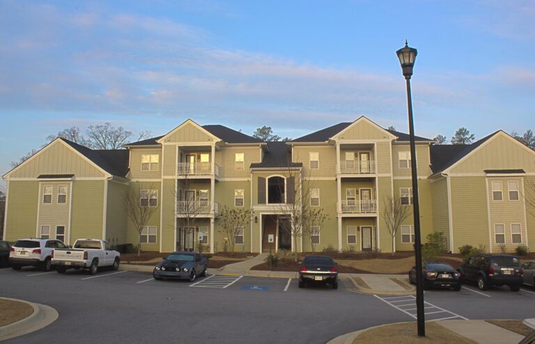 A large apartment complex named Woodland Trail with a parking lot filled with cars.